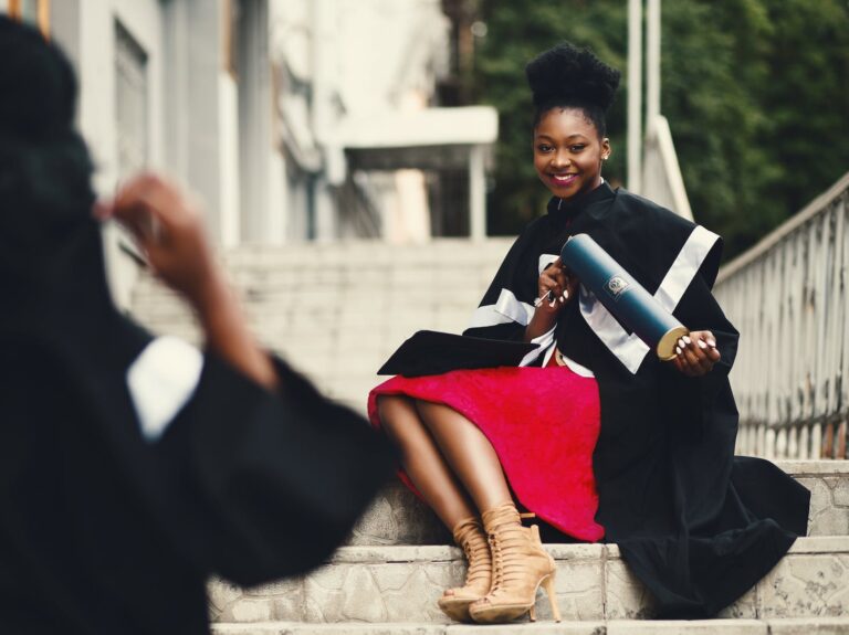 woman wearing black graduation coat sits on stairs