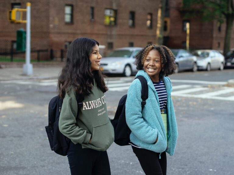 happy multiethnic girlfriends with backpacks speaking on city road