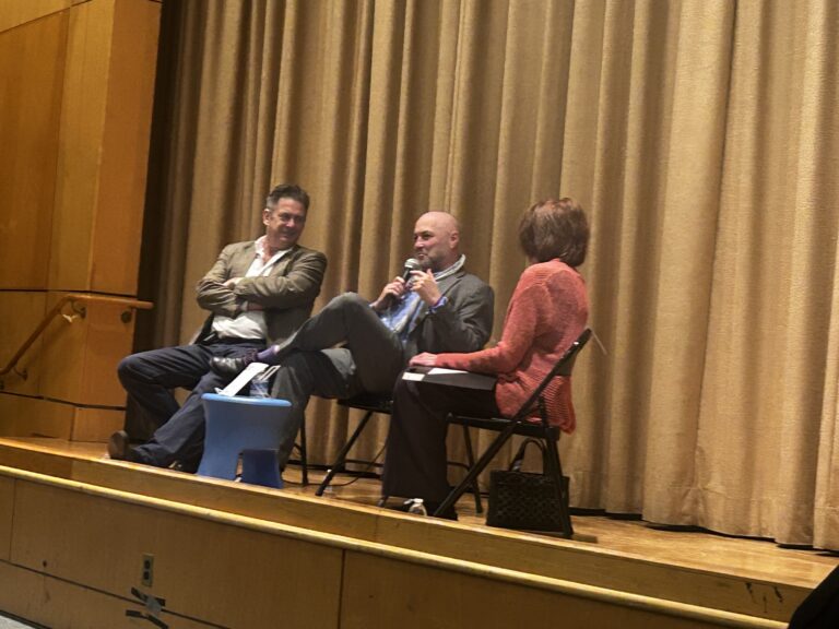 Writer Colum McCann sits on a stage flanked by writer Ed Conlan and Friends of the Crestwood Library President Cathleen Walsh.